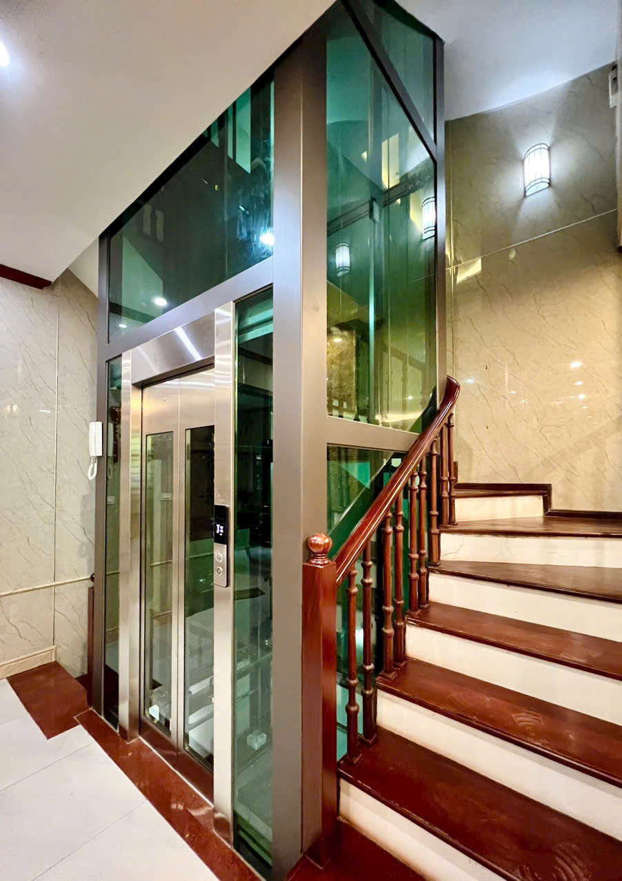 Thang máy gia đình vách kính cạnh cầu thang gỗ trong nhà sang trọng